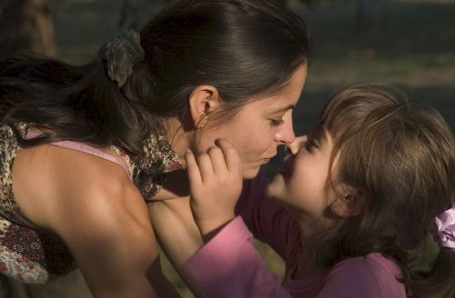 Moment de tendresse entre une fille et sa maman. Nez contre nez, elles s’apprêtent à s’embrasser. Elles sont complices et heureuses.