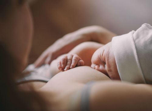 Maman allaitant son nouveau-né, yeux fermés, avec son bonnet de naissance sur la tête. 